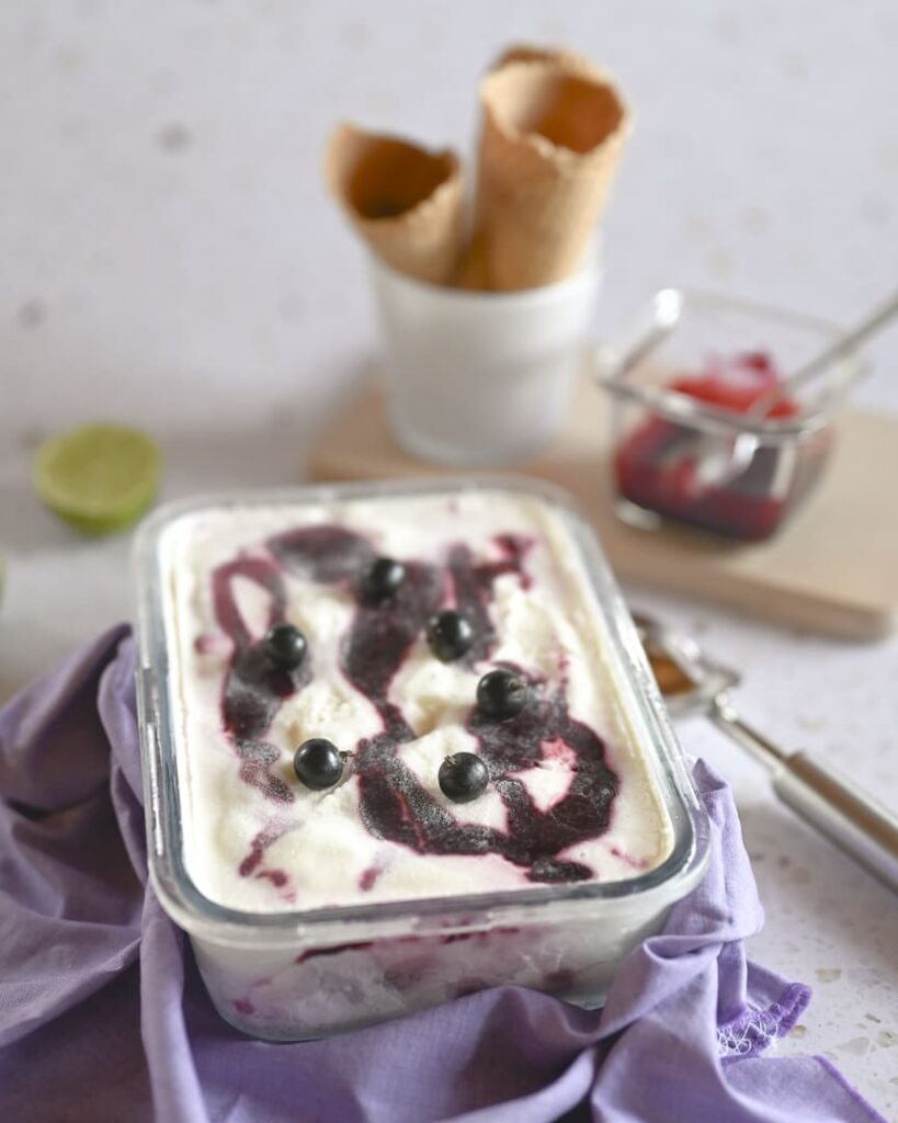 Frozen Joghurt mit Johannisbeer-Swirl und frischen Beeren Frozen Joghurt in einer Glasform mit Johannisbeer-Swirl und schwarzen Johannisbeeren auf lila Tuch
