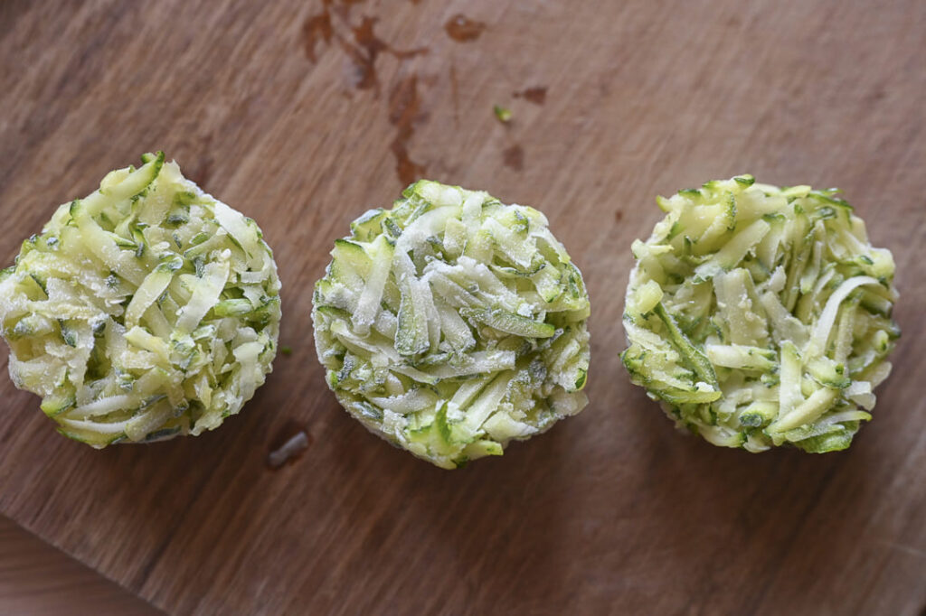 Zucchini geraspelt und portioniert einfrieren – praktische Vorratshaltung Zucchini einfrieren: Drei gefrorene Portionen geraspelter Zucchini auf einem Holzbrett