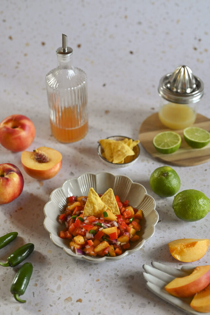 Sommerliche Nektarinen-Salsa in einer Schale mit Nachos, frischen Limetten, Paprika und Jalapeños – fruchtig-scharfes Rezept.