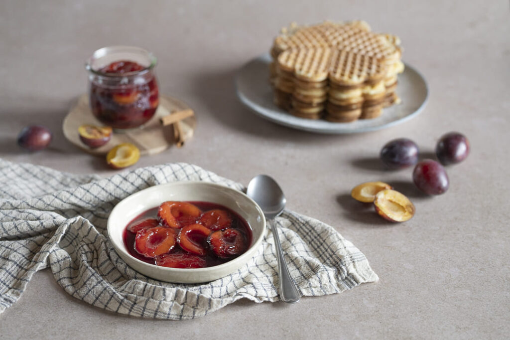 Hausgemachter Zwetschgenröster in einer Schale, serviert mit Waffeln und frischen Zwetschgen