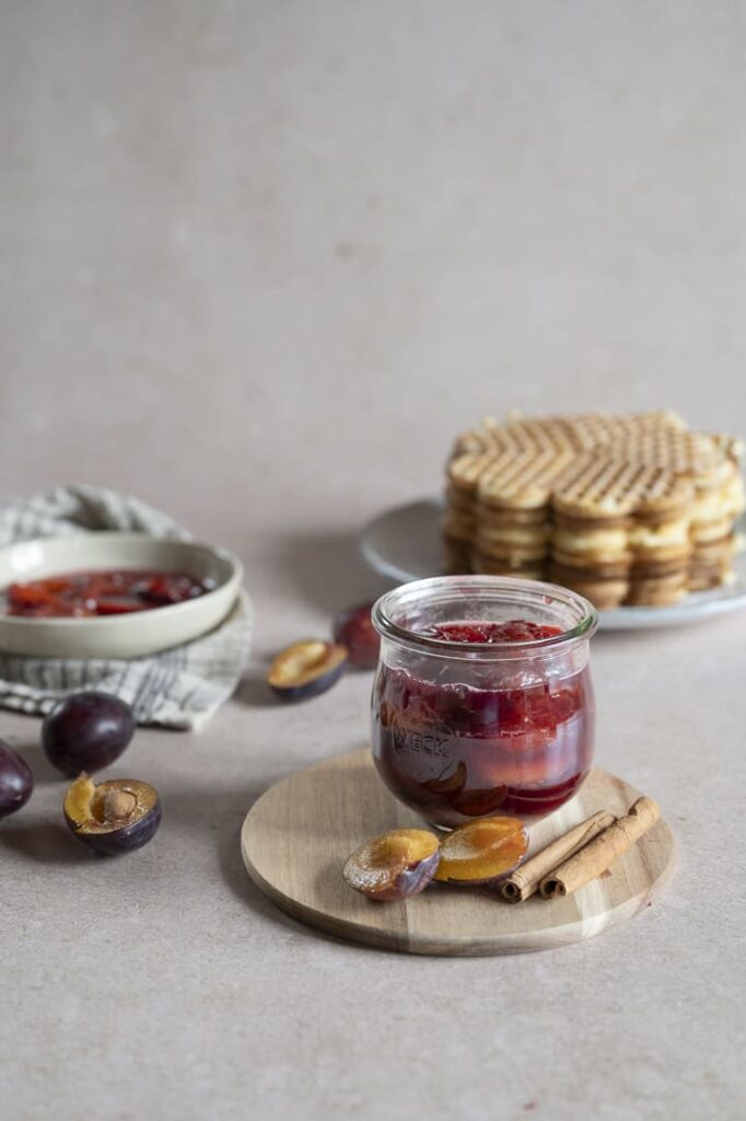 Eingekochter Zwetschgenröster im Glas mit frischen Zwetschgen und Zimtstangen, serviert mit Waffeln