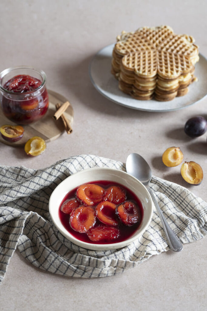 Hausgemachter Zwetschgenröster in einer Schale serviert, dazu frische Zwetschgen und Waffeln