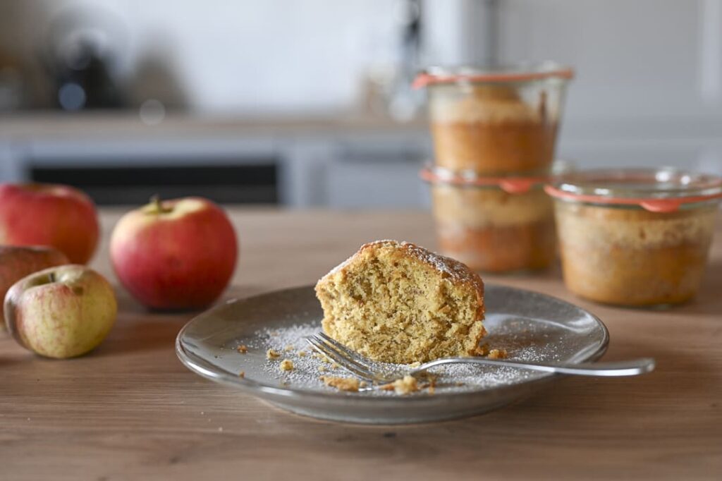 Apfel-Nuss-Kuchen im Glas – saftiger Kuchen auf Teller mit frischen Äpfeln und eingekochten Gläsern im Hintergrund